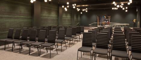 A conference room with rows of chairs, a podium, and a projector screen.