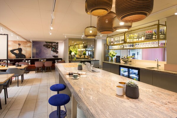 A modern bar area with a marble countertop, blue bar stools, and hanging wicker light fixtures.