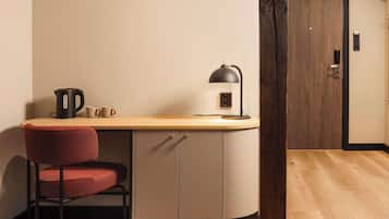 A compact kitchenette with a wooden countertop, a kettle, a coffee maker, and a chair.