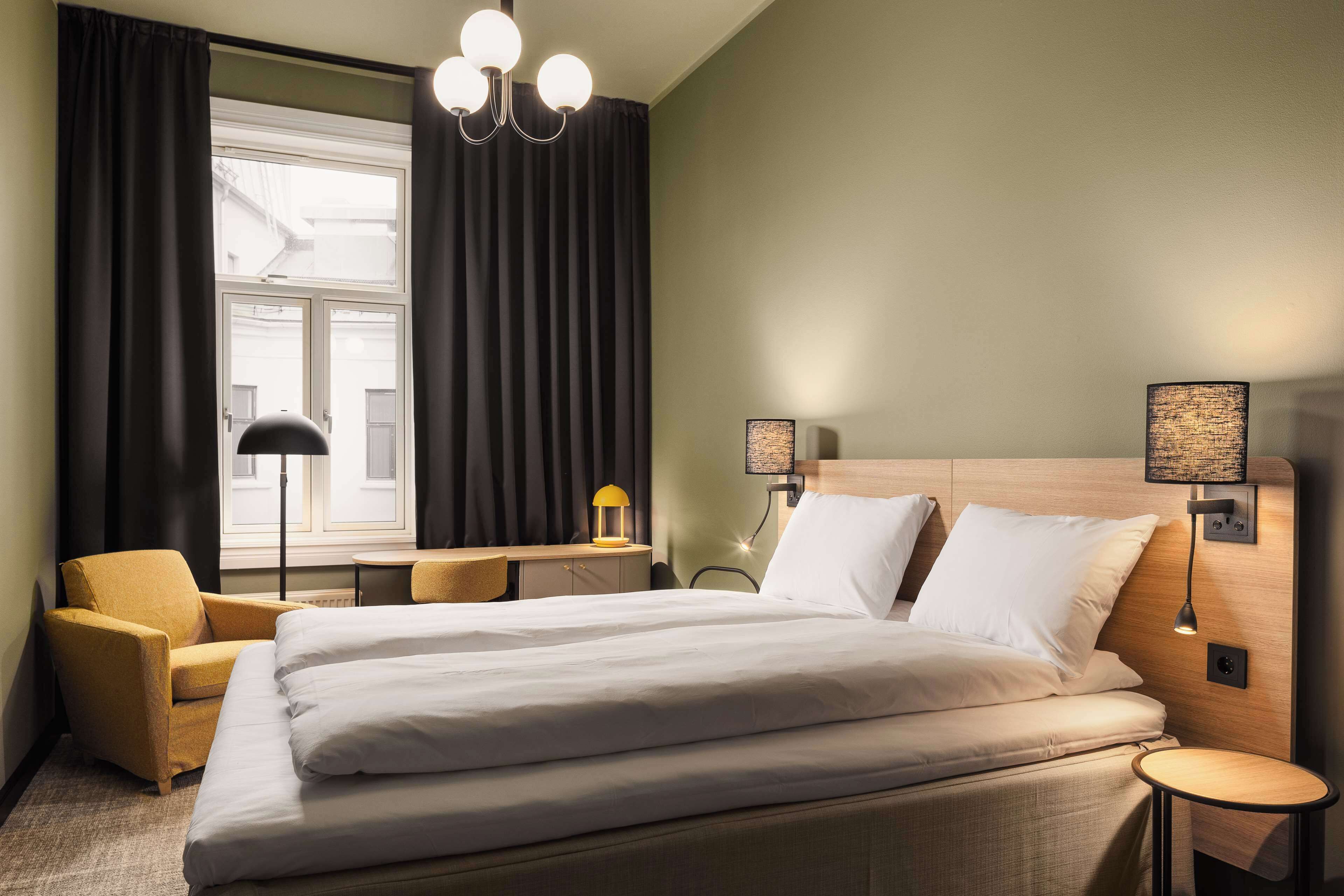A hotel room with a large bed, a desk, a chair, and two bedside lamps.