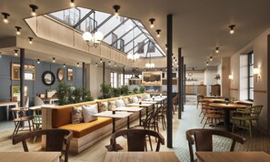 A spacious cafe with a long wooden bench seating area, a kitchen in the background, and a skylight above. - Scandic Holberg (Oslo)