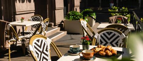 An outdoor cafe with wicker chairs, tables, and a variety of pastries.