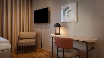 Una habitación de hotel con una cama, un escritorio con una lámpara, una silla, un televisor y una obra de arte enmarcada en la pared.
