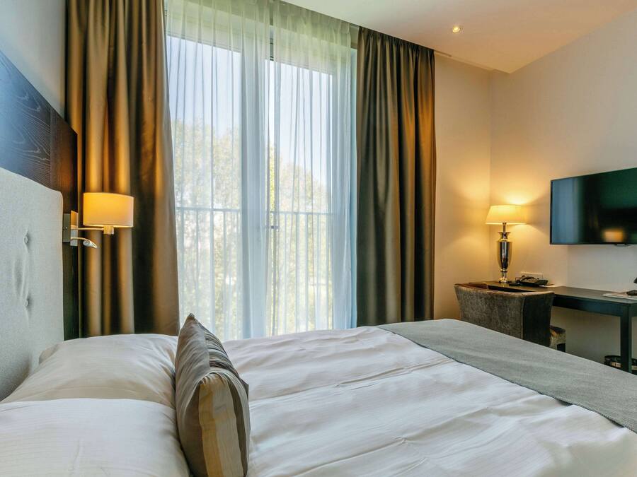 A hotel room with a large bed, a desk, a chair, a TV, and curtains.