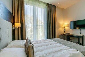 A hotel room with a large bed, a desk, a chair, a TV, and curtains.