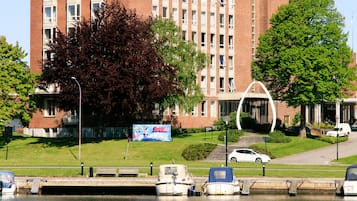 A multi-story brick building with a clock tower, surrounded by a grassy area and a body of water.
