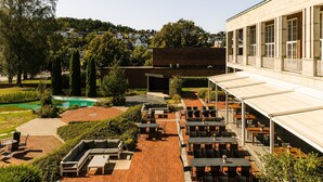 Un espacio de patio con mobiliario exterior, piscina y un edificio con grandes ventanales.