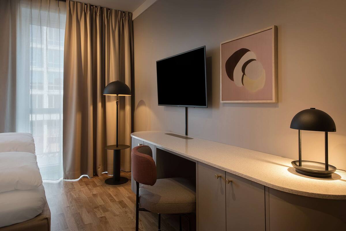 A hotel room with a bed, a desk, a chair, a TV, and a lamp.