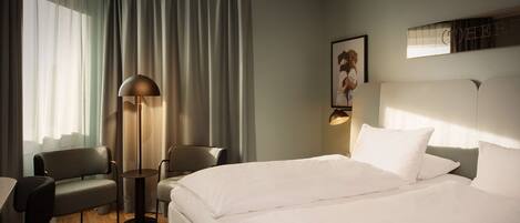 A hotel room with a bed, two chairs, a floor lamp, and a large window with curtains.