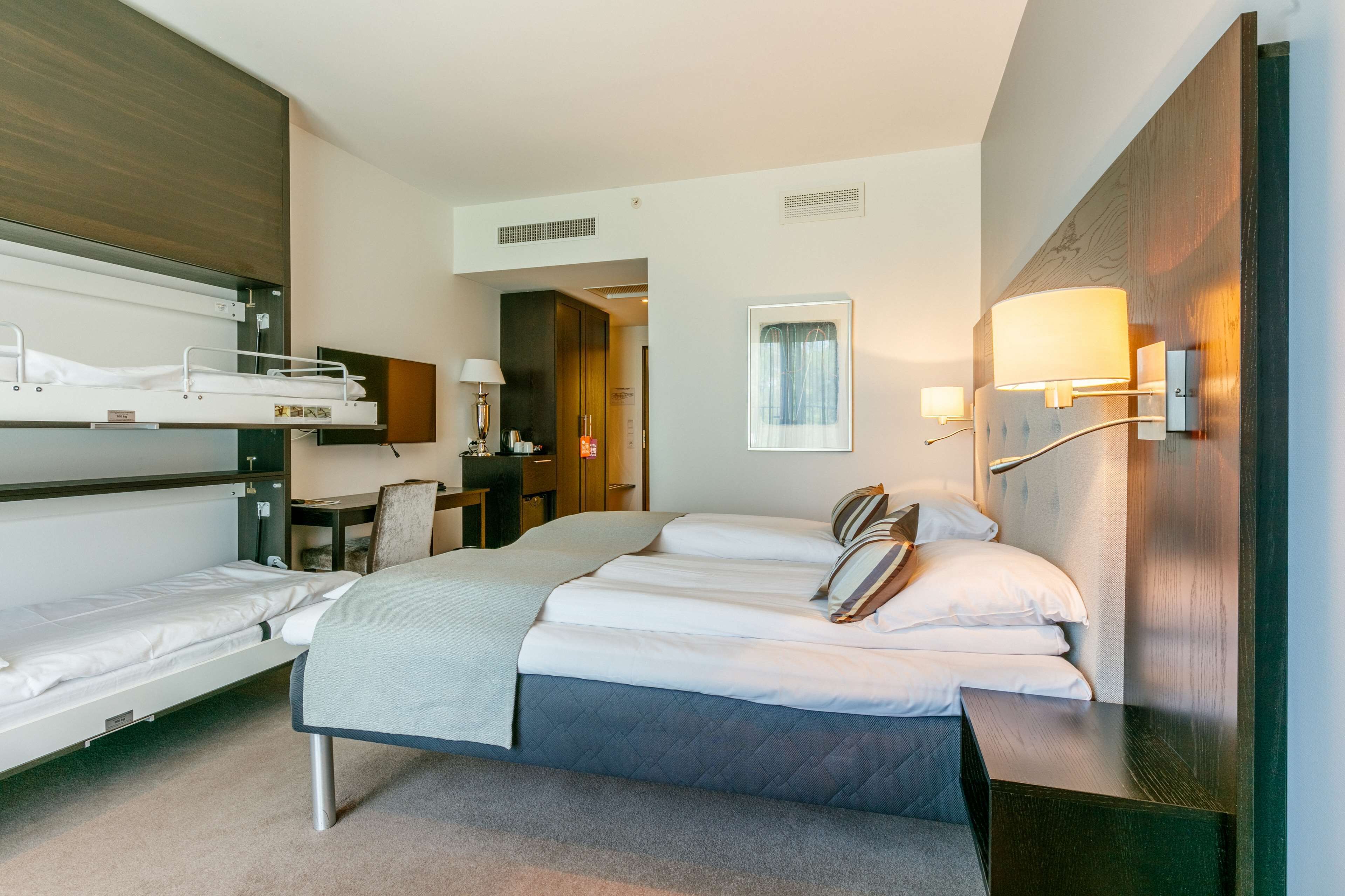 A hotel room with a large bed, a desk, a chair, a wardrobe, and a bunk bed.