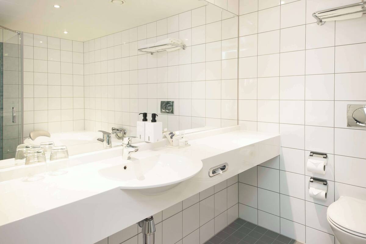 A modern bathroom with a large mirror, two sinks, a toilet, and a shower area.