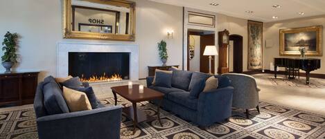 A spacious living room with a fireplace, sofas, a piano, and a large painting.