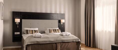 A modern bedroom with a large bed, two bedside tables with lamps, a dark headboard, and a large window with sheer curtains.