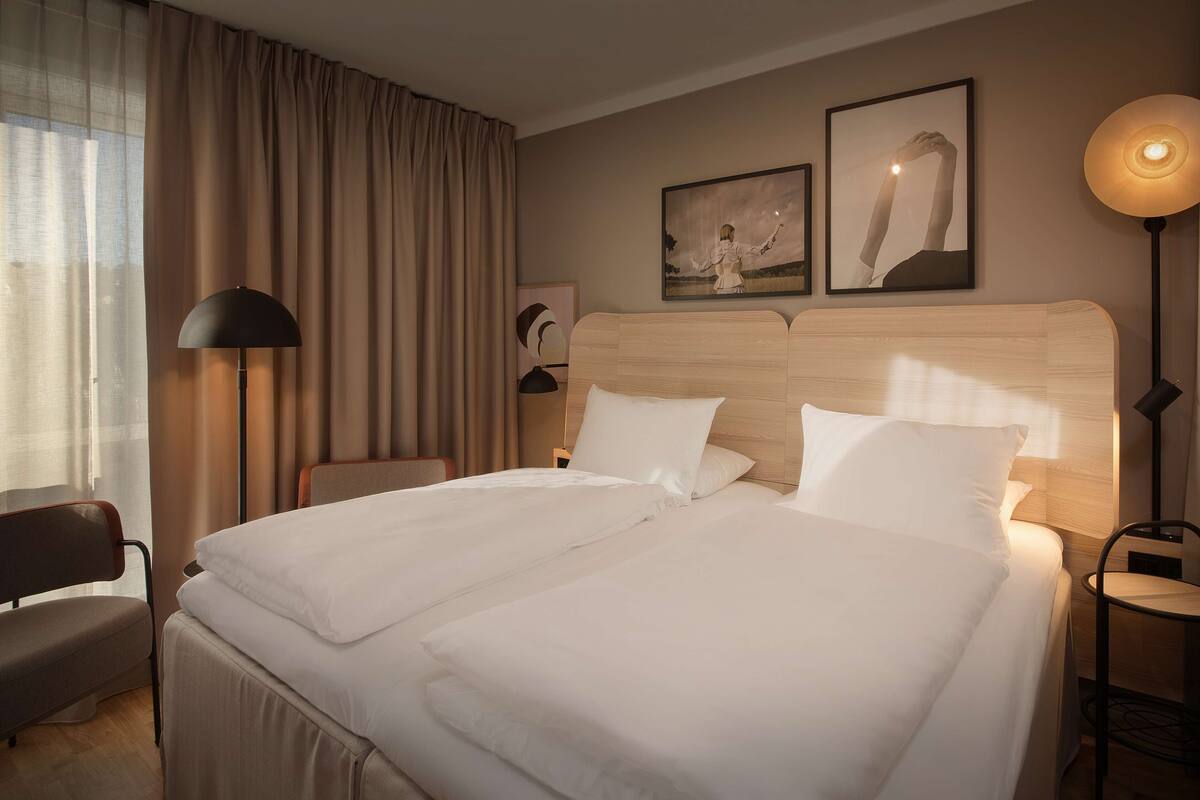 A hotel room with a large bed, a chair, a desk, and a lamp.