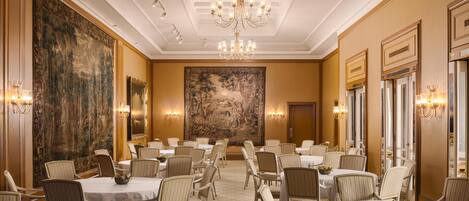 A formal dining room with round tables, chairs, and a large painting on the wall.