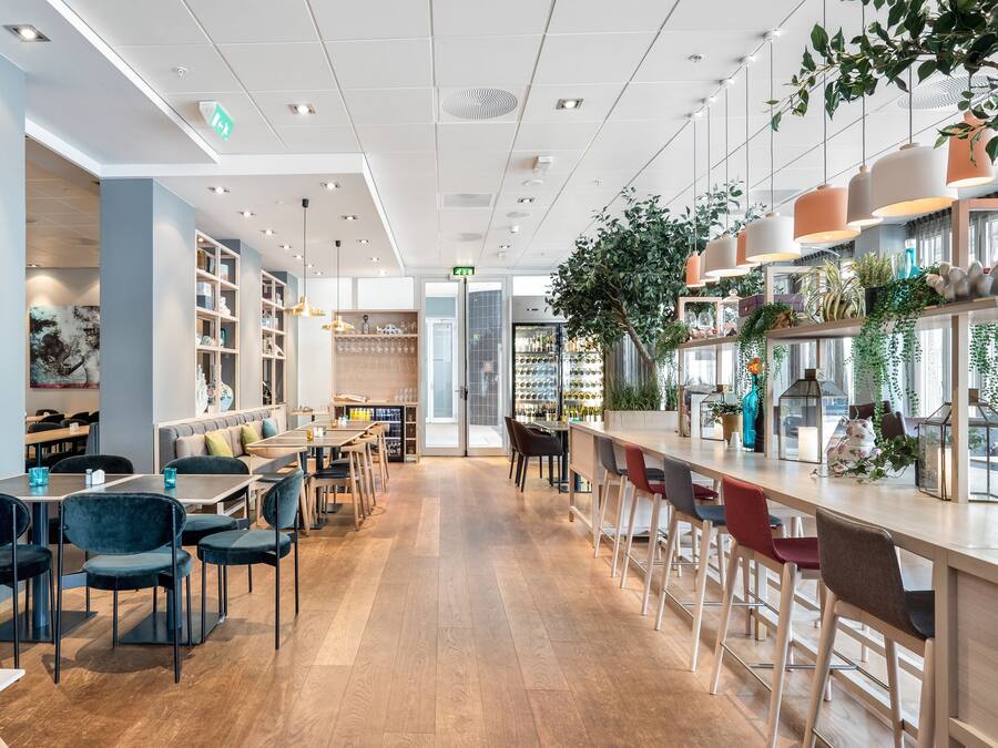 Un café moderno con pisos de madera, asientos en la barra y una variedad de plantas.