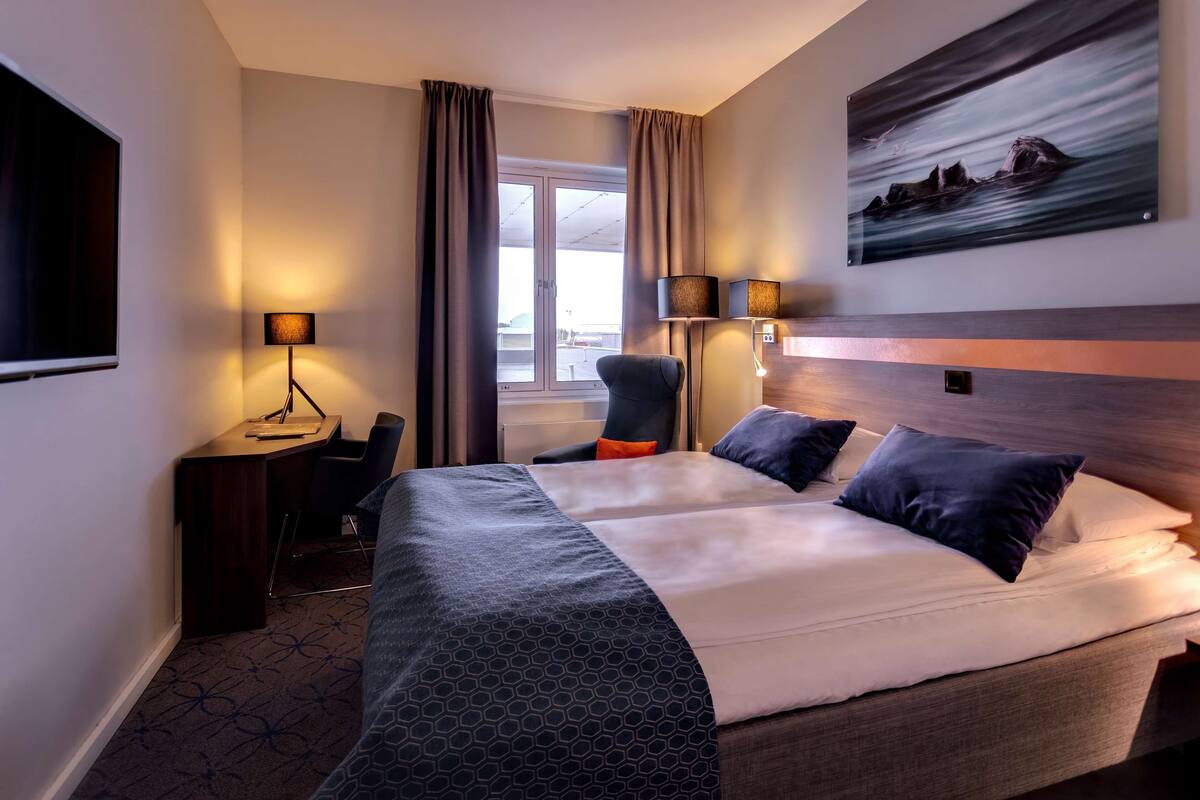 Une chambre d’hôtel avec un grand lit, un bureau, une chaise, une télévision et un tableau au mur.