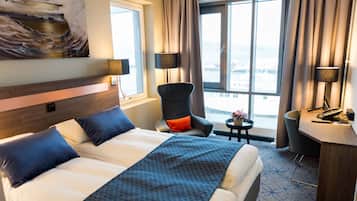 Habitación de hotel con una cama grande, dos sillas, un escritorio y vistas a la ciudad.