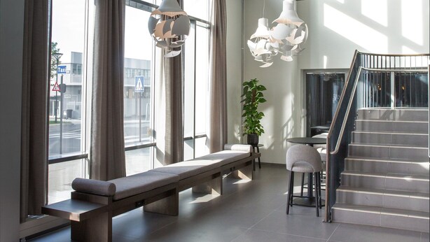 Een ruime lobby met grote ramen, een trap en modern hanglicht.