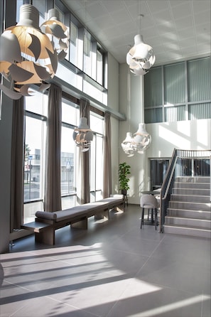 A spacious lobby with large windows, a staircase, and modern pendant lighting.