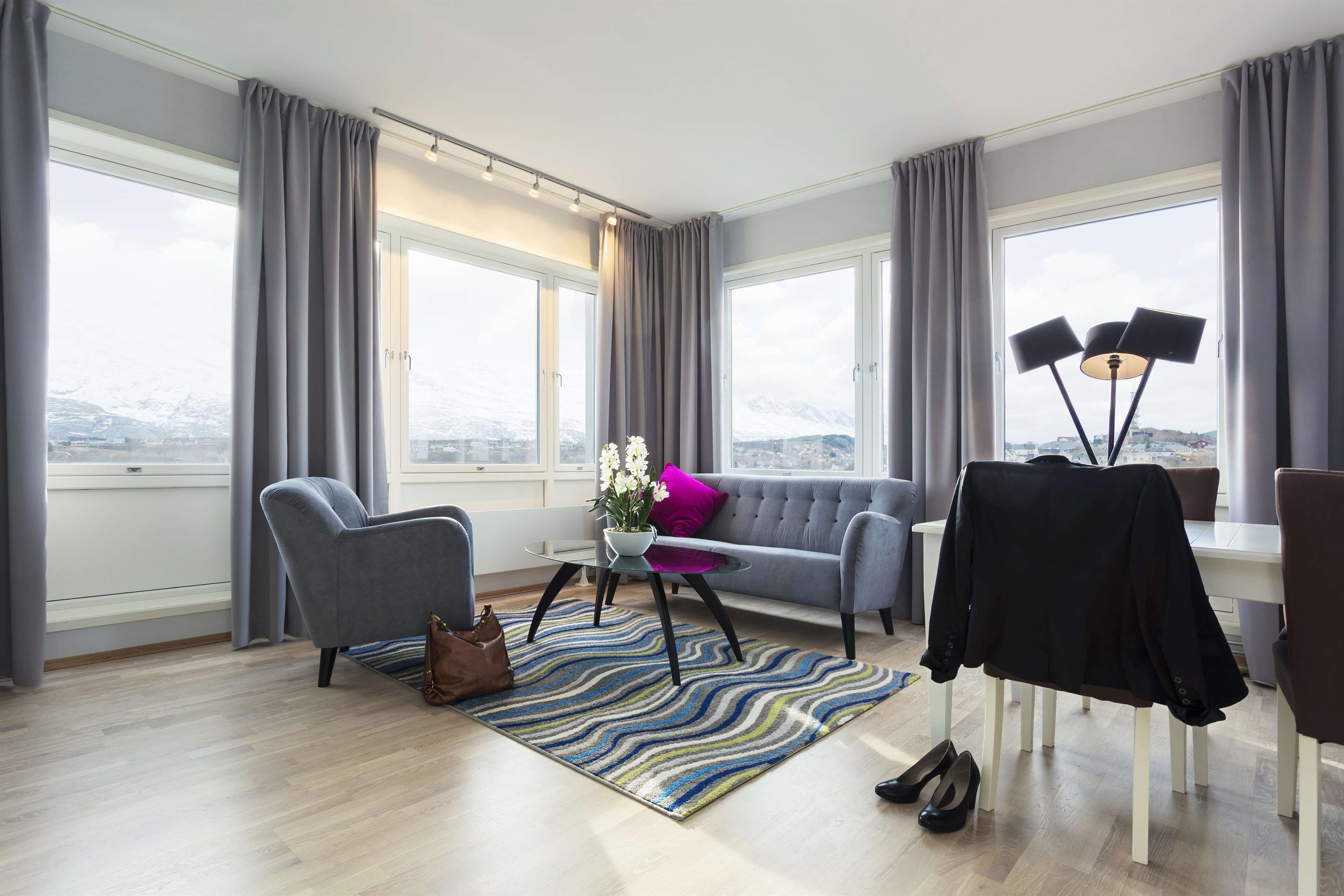 Ett modernt vardagsrum med en grå soffa, två fåtöljer, ett soffbord och en utsikt över snöklädda berg genom stora fönster.
