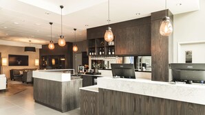 Een moderne bar met een houten toonbank, hanglampen en een barstation met een beeldscherm.