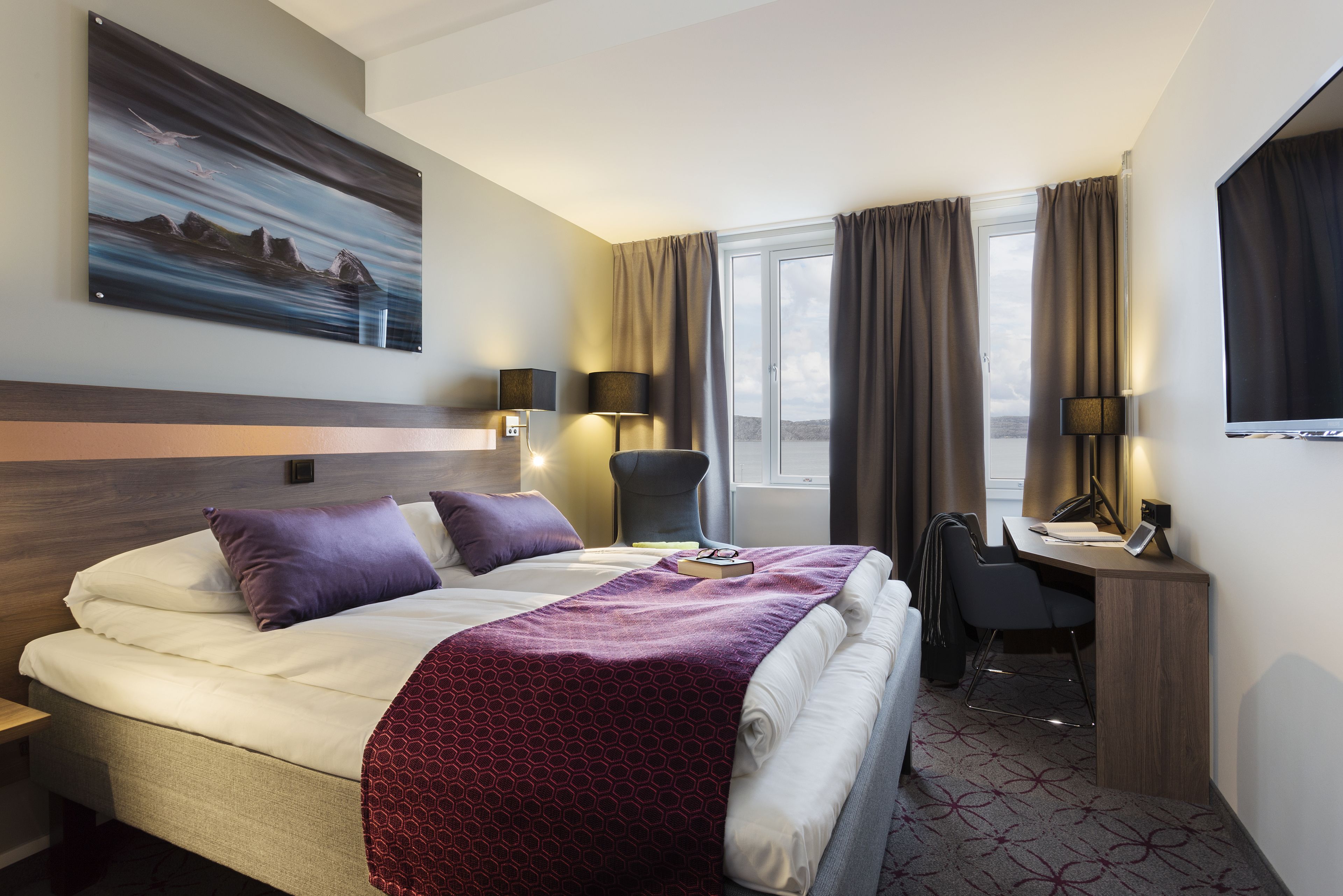 Ett hotellrum med en säng, ett skrivbord, en stol och en tavla på väggen.