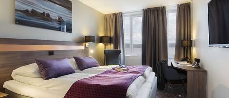 Ett hotellrum med en säng, ett skrivbord, en stol och en tavla på väggen.
