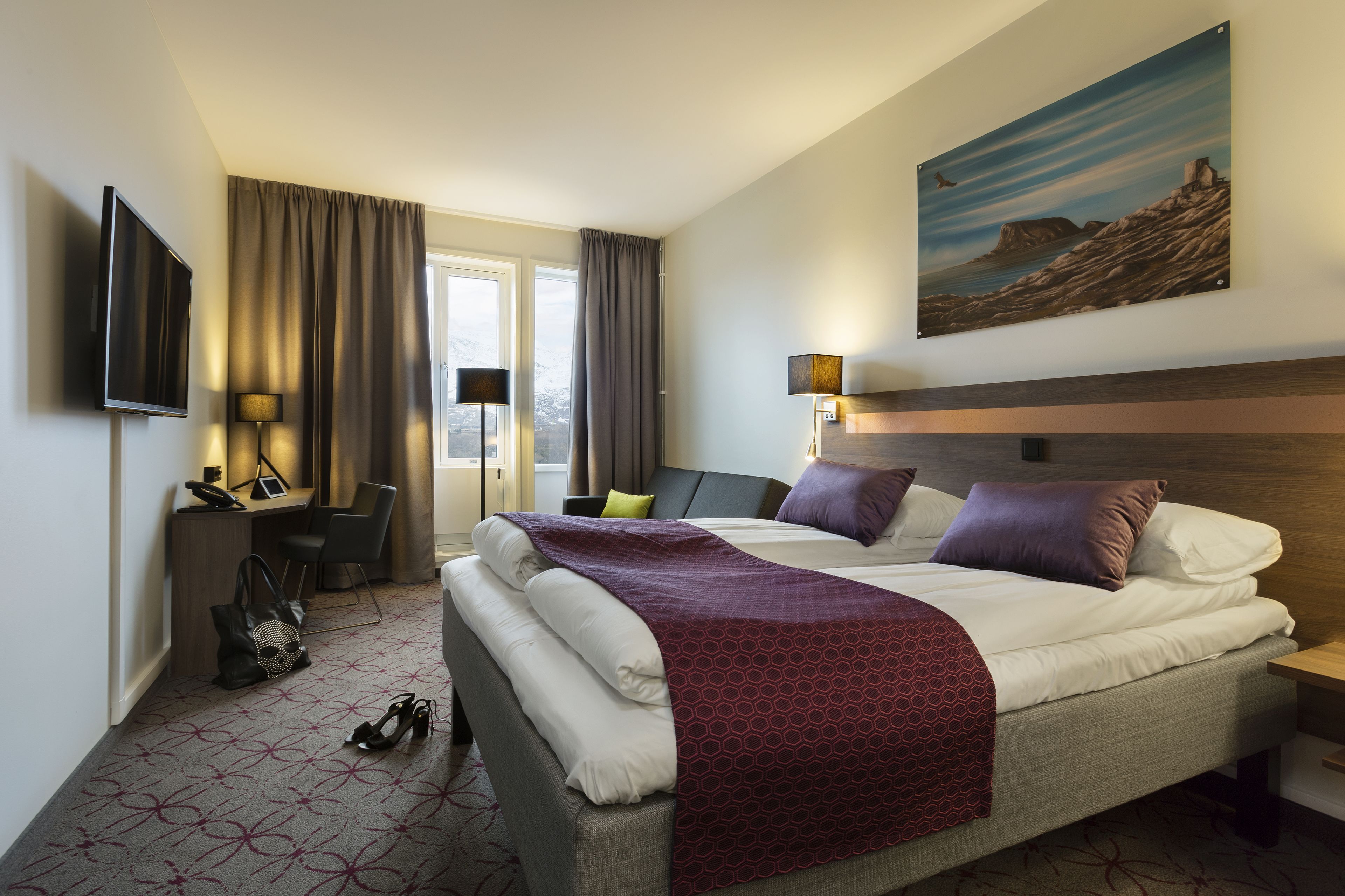 Ein Hotelzimmer mit Bett, Schreibtisch, Stuhl, Fernseher und Kunstwerk an der Wand.