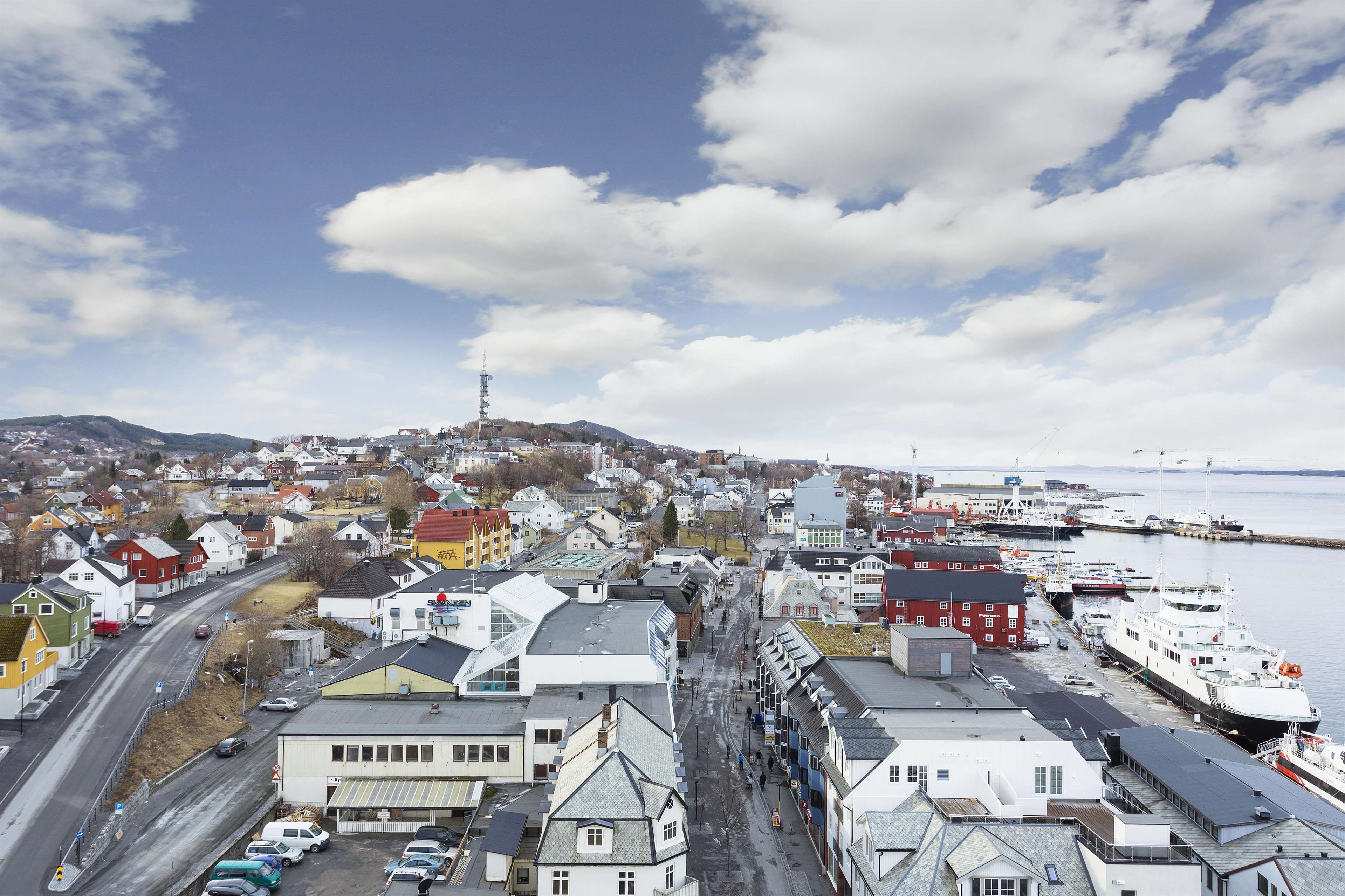 A coastal town with a mix of residential and commercial buildings, a prominent hill, and a marina with boats.
