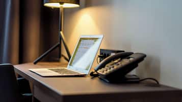 A laptop on a desk with a telephone and a lamp in the background.