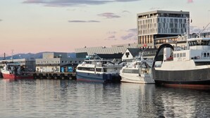 Een haven met meerdere boten afgemeerd, een modern gebouw met glazen gevel en een heldere lucht.