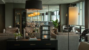 Een moderne hotel lobby met een donkergrijze zithoek, een centrale salontafel met decoratieve objecten, en een groot raam met uitzicht op de stad.