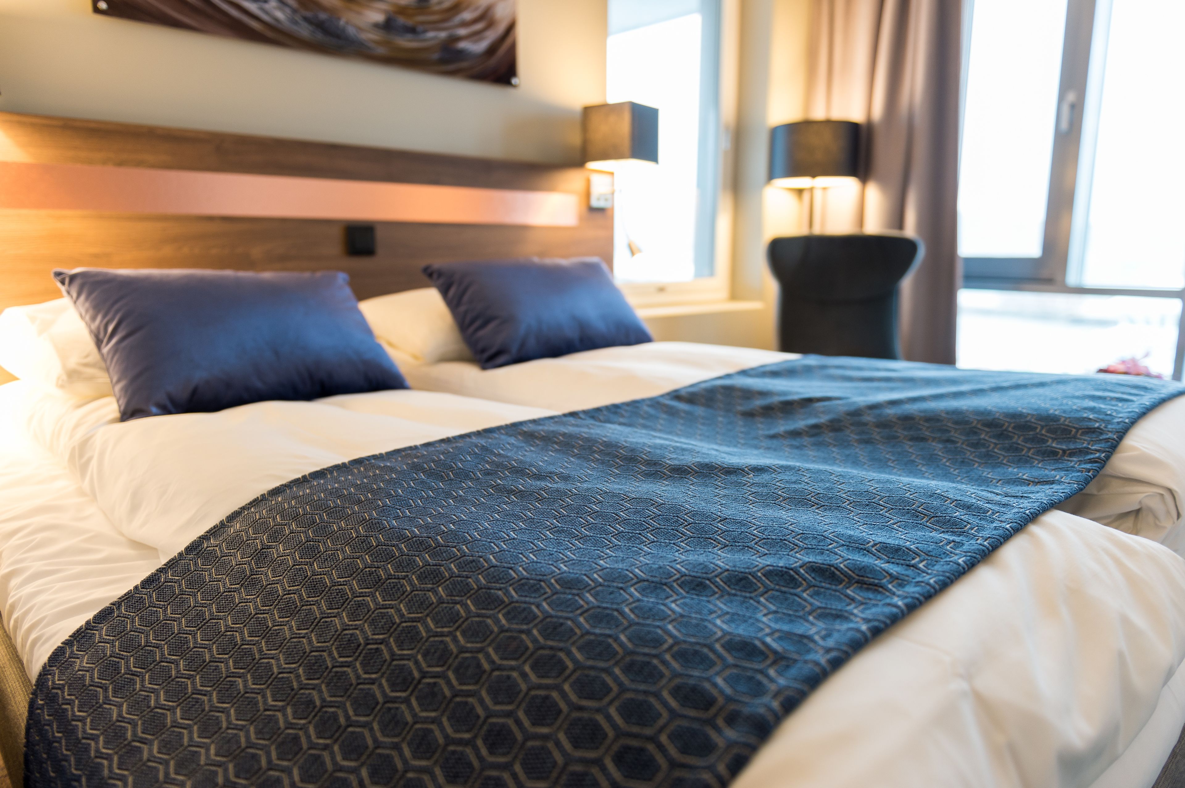 A neatly made bed with a patterned blanket, a headboard, and a bedside lamp.