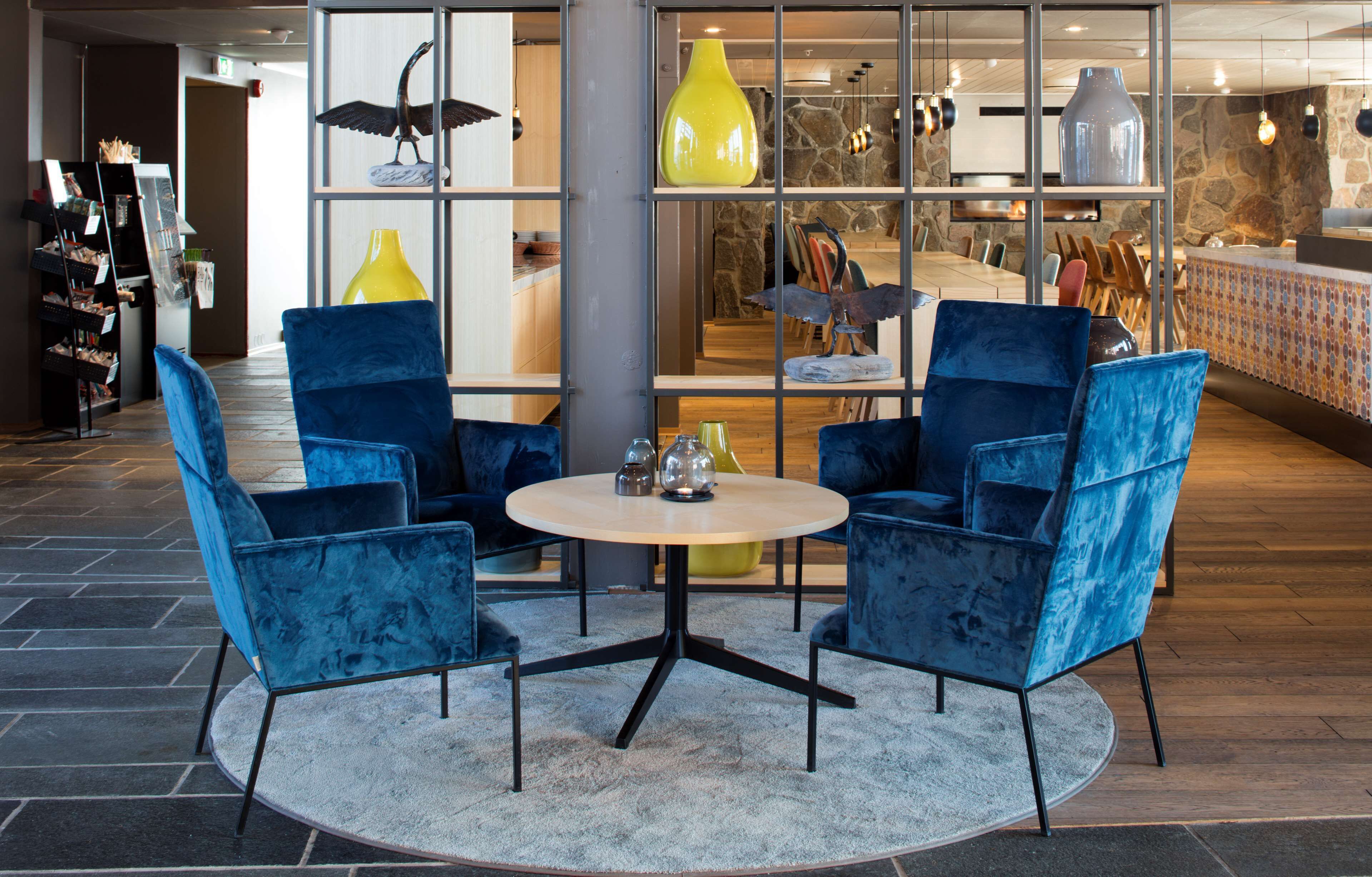 A modern interior with a round table and two blue chairs, a yellow vase, and a stone wall with a wooden counter.