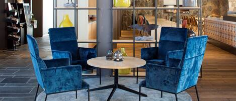 A modern interior with a round table and two blue chairs, a yellow vase, and a stone wall with a wooden counter.