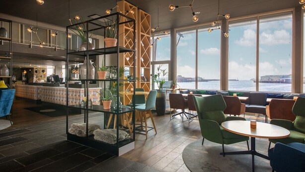 Um interior moderno com área de bar, assentos e amplas janelas com vista para um corpo de água.
