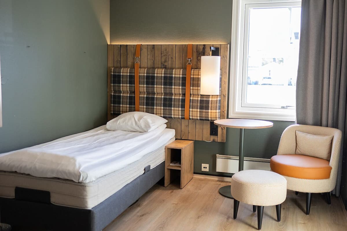 A compact hotel room with a single bed, a small bedside table, a chair, and a round table.