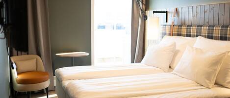 Habitación de hotel con una cama grande, una silla, una mesita y una ventana con cortinas.