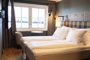 A hotel room with a large bed, a round table, a chair, and a window with curtains.