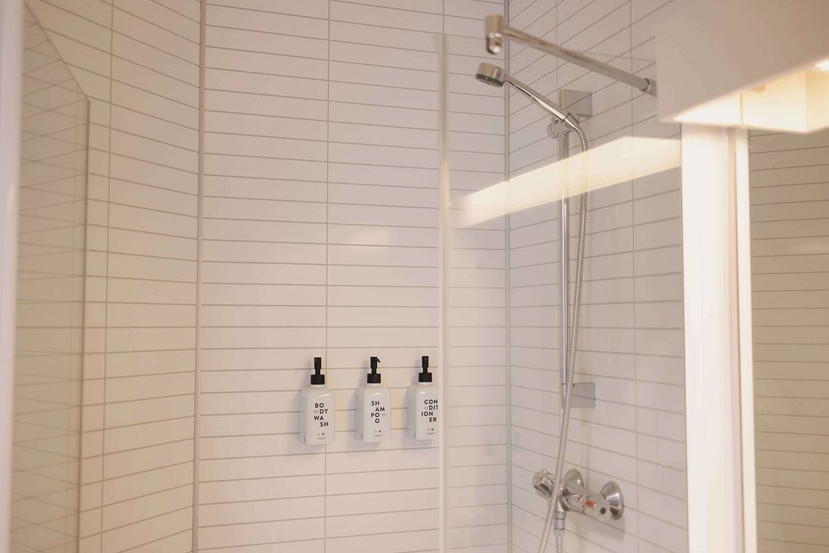 A bathroom with a shower, tiled walls, and three bottles of toiletries on the wall.