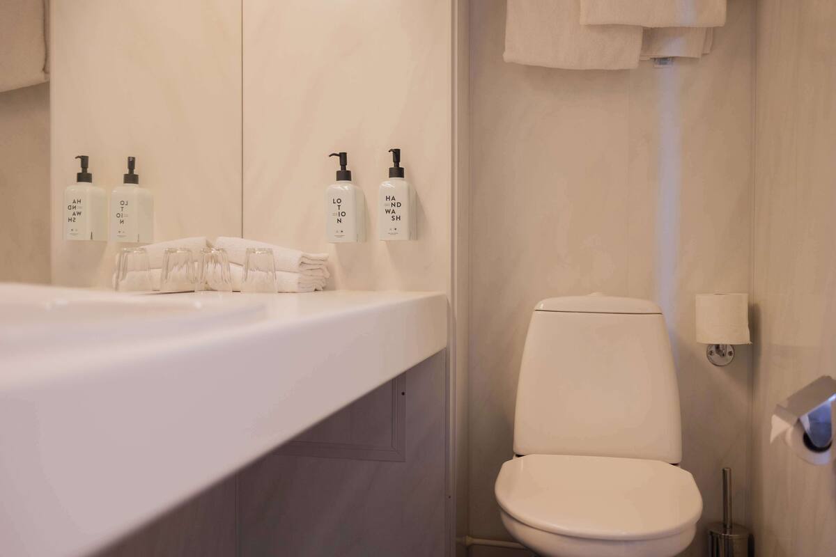 A bathroom with a white sink, two hand soap dispensers, a toilet, and a paper towel dispenser.