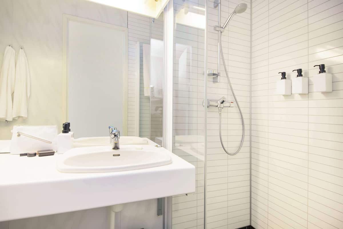 A modern bathroom with a white sink, a glass-enclosed shower, and toiletries on the wall.