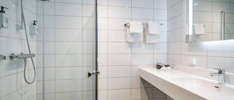 A modern bathroom with a glass-enclosed shower, white tiled walls, a large mirror, and a white countertop with a sink.