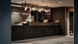 A reception area with a modern design, featuring a reception desk, a sign reading "GRAND TROMSO", and a staircase leading to an upper level. - Quality Hotel Grand Tromso (Tromso)