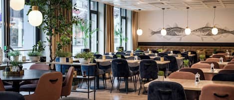 Un interno di ristorante moderno con tavoli e sedie in legno, piante in vaso e illuminazione a sospensione.
