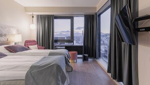 A hotel room with two beds, a red chair, a desk with a TV, and a large window with curtains. - Quality Hotel Grand Tromso (Tromso)