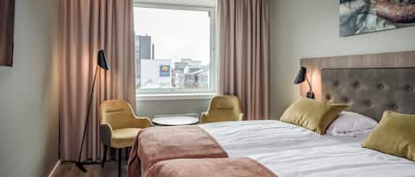 A hotel room with a bed, two chairs, a small table, and a window with curtains.