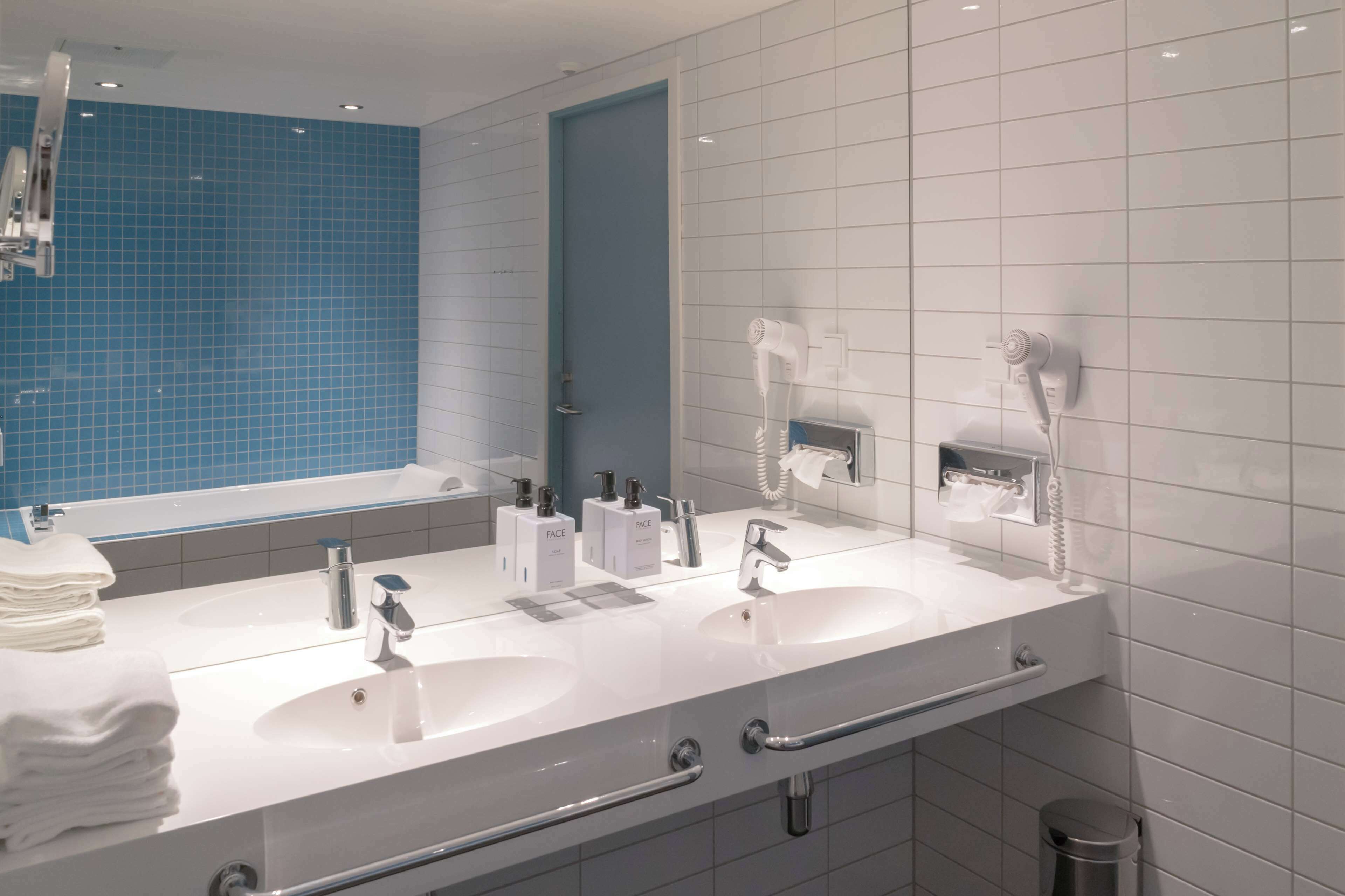 A modern bathroom with two sinks, a large mirror, and a blue-tiled wall.