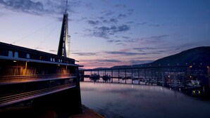 A waterfront view with a modern building, a dock with boats, and a mountain in the background. - Scandic Ishavshotel (Tromsø)